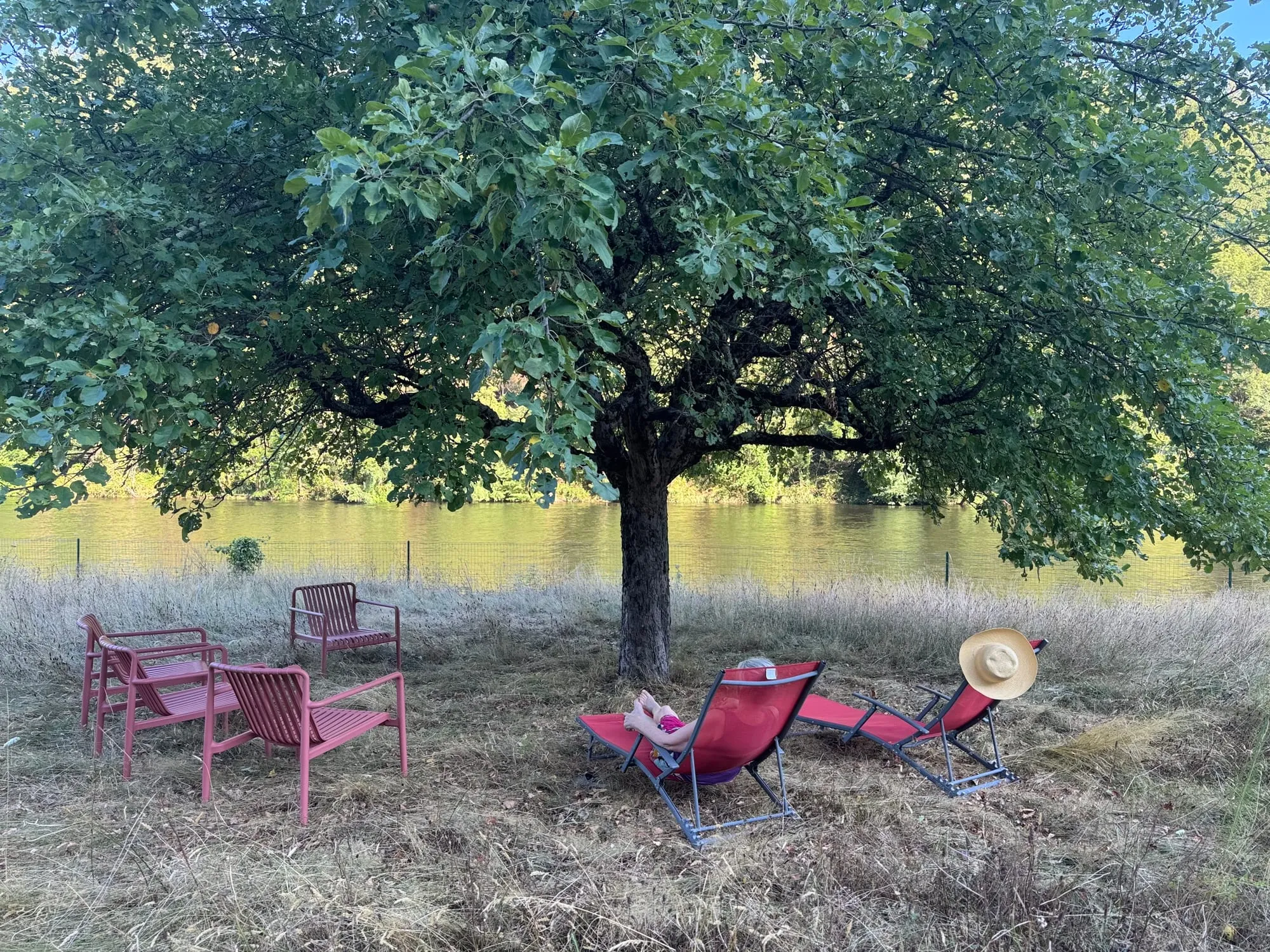 Transats et fauteuils rouges à l’ombre d’un pommier, au bord de la Truyère